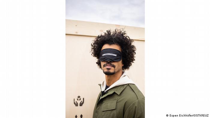 Der Künstler Philip Kojo Metz trägt eine schwarze Binde mit einem Schriftzug über den Augen.