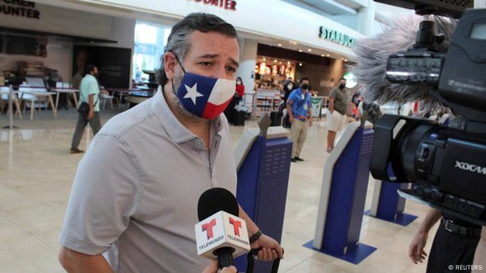 Le sénateur Ted Cruz portant un masque de drapeau du Texas et interviewé par les médias dans un aéroport