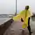 Woman walking in a yellow rain cape along a sidewalk with Kara Tepe camp in the background