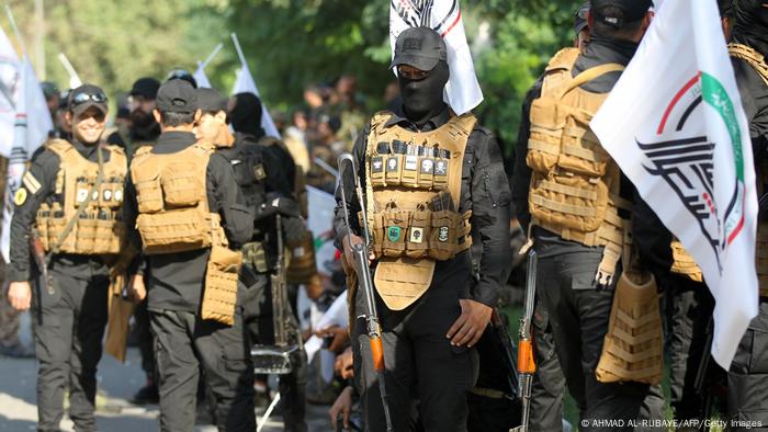 Members of Iraqi paramilitary holding guns and flags, stand guard during a funerary procession in Baghdad.