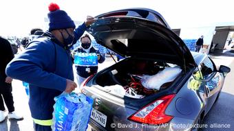 A man puts packs of bottled water into the trunk of his car