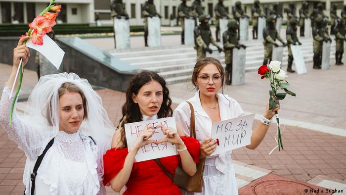 A photograph from the exhibition The Future of Belarus, Fueled by Women. 24-year-old Anna stands with two young women. She wears a wedding dress and veil that belong to her mother, who got married 26 years ago. Lukashenko has been president of Belarus since then. The picture was taken by photographer Nadia Buzhan.