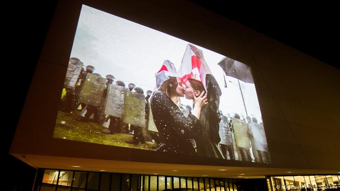 Im Rahmen der Ausstellung The Future of Belarus, Fueled by Women im MO Museum in Vilnius, Litauen, werden die ausgestellten Fotografien auf die Außenwand des Museums projiziiert. Auf dem hier projiziierten Foto ist zu sehen, wie sich zwei junge Demonstrantinnen unter einer weißrussischen Fahne küssen. Das Museum ist aufgrund der Lockdown-Bestimmungen wegen der COVID 19-Pandemie für Besucherinnen und Besucher geschlossen.