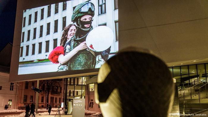 Im Rahmen der Ausstellung The Future of Belarus, Fueled by Women im MO Museum in Vilnius, Litauen, werden die ausgestellten Fotografien auf die Außenwand des Museums projiziiert. Auf dem hier projiziierten Foto ist zu sehen, wie eine demonstrierende Frau im roten Kleid einen Soldaten in Uniform umarmt. Das Museum ist aufgrund der Lockdown-Bestimmungen wegen der COVID 19-Pandemie für Besucherinnen und Besucher geschlossen.