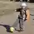 Mališan igra nogomet na prašnjavoj ulici