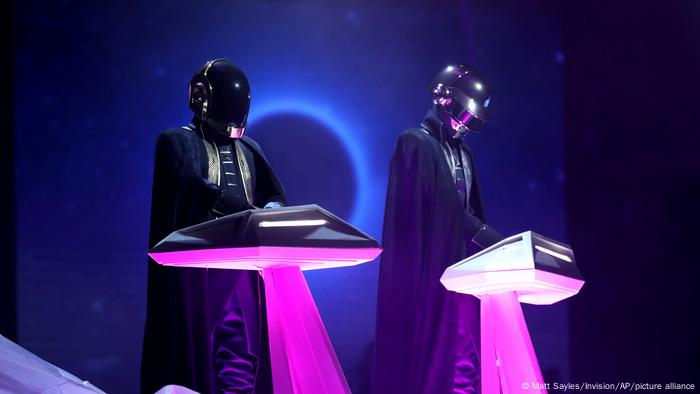  Daft Punk, two performers in space costume, standing behind consoles.