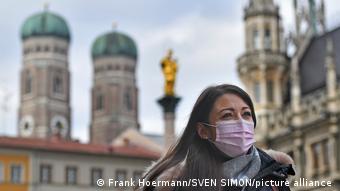Женщина в маске стоит на фоне Фрауэнкирхе в Мюнхене