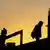 People looking weary, wearing masks and silhouetted against the dawn light