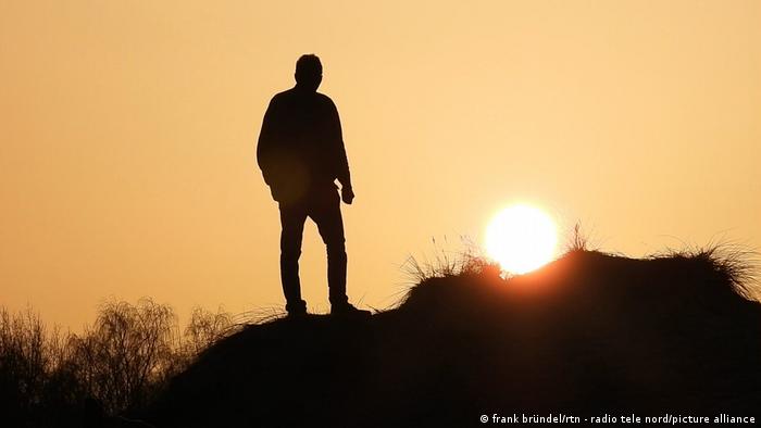 Man standing on a sand dune in front of the sunrise.