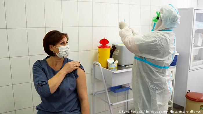 A woman rolls up her sleeve to get a COVID-19 vaccination