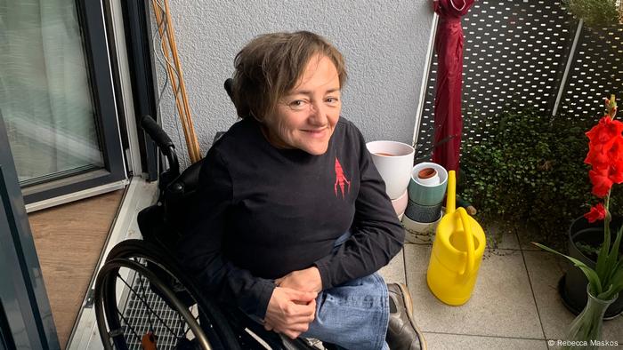 Rebecca Maskos sitzt im Rollstuhl auf einem Balkon und schaut in die Kamera