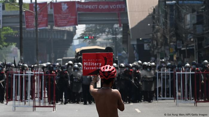 Ein einzelner Mann mit einem Protestschild steht auf einer Straße in Yangon, Myanmar, bewaffneten Sicherheitskräften gegenüber Ein einzelner Mann mit einem Protestschild steht auf einer Straße in Yangon, Myanmar, bewaffneten Sicherheitskräften gegenüber
