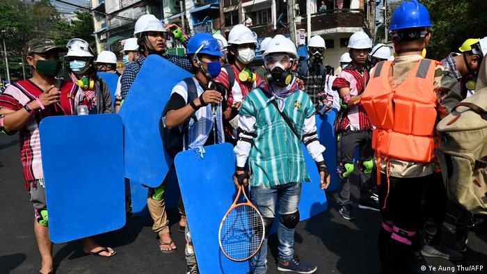 Protesters hold rackets and blue homemade shields. They are wearing helmets.