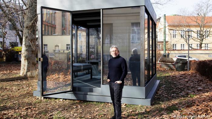 Can Dündar standing outside in front of the glass box which is part of the installation.