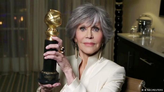 Jane Fonda hält einen goldenen Preis mit schwarzem Sockel in die Kamera und lächelt.