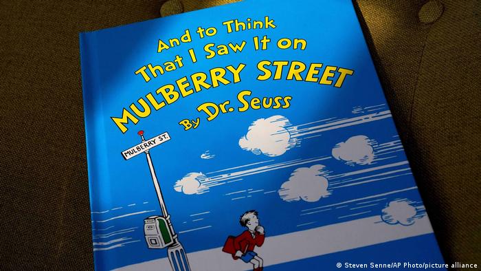 The book cover of the Dr. Seuss work And to think that I saw it on Mulberry Street. It shows a boy dressed in a red blazer and blue shorts standing next to a Mulberry street sign.