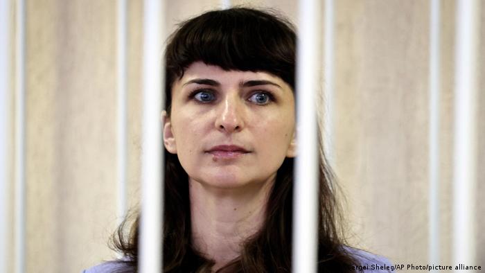 A woman with long dark hair sits behind bars