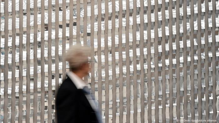 A museum visitor walking past a wall-sized work of art which reflects light.