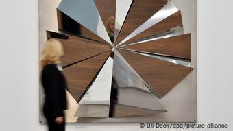 A woman walks in front of a reflective sculpture titled 'Silver Fan.'