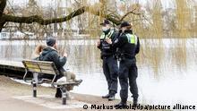 Polizisten sprechen an Hamburgs Aussenalster ein Paar an, weil sie auf der Bakn sitzend keinen Mund-Nasen-Schutz trugen. Seit gestern gilt in Hamburg eine verschärfte Maskenpflicht im öffentlichen Raum.