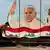  Iraqi municipal workers sweep a street in front of a giant board covered with a painting of Pope Francis.