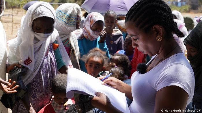 A woman looks at a notebook and pen as a crowd gathers around.