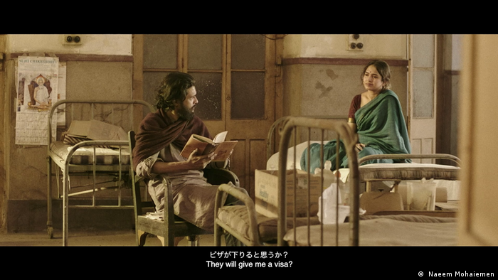 A film still showing a man reading out from a book to a woman at a hospital