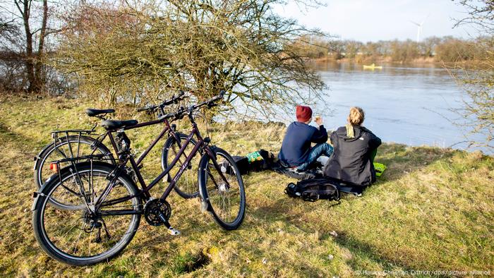 A couple sitting on the banks of a river in front of their bicycles in Germany A couple sitting on the banks of a river in front of their bicycles in Germany