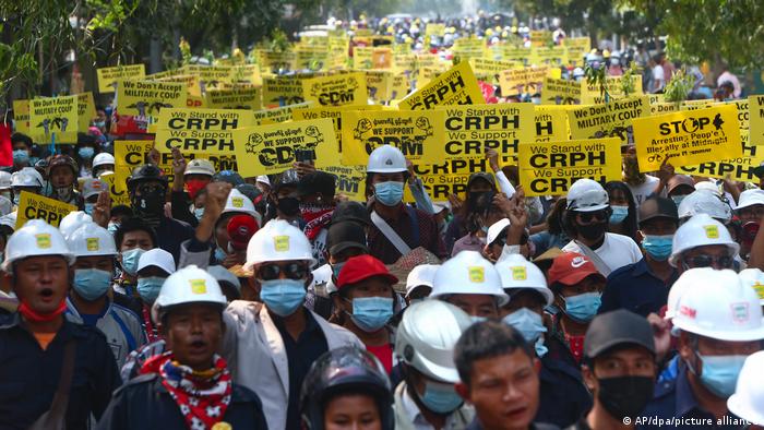 Demonstration in Mandalay gegen den Militärputsch. Die Demonstranten tragen mehrheitlich Schutzhelme und medizinische Gesichtsmasken. Die Demonstranten in der hinteren Bildhälfte tragen Schilder Stand with CRPH / We support CRPH 