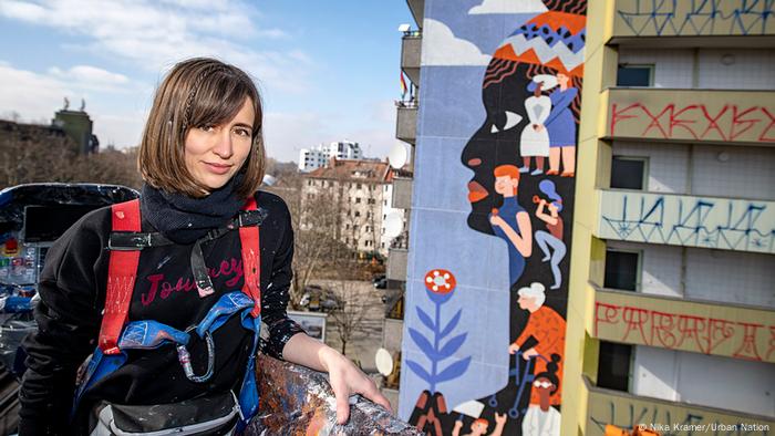 Artista Kate Voronina em frente a painel de Marielle