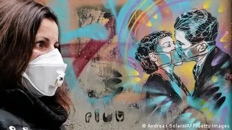 A work of graffiti depicts a couple kissing while wearing masks.