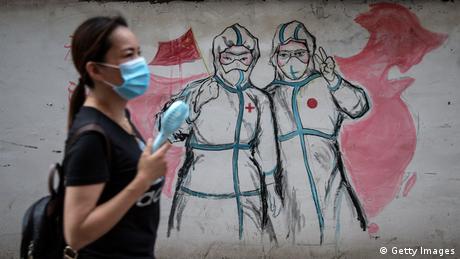 A woman walks by a graffiti painting on the wall depicting two nurses; one holding a Chinese flag and the other making a peace sign.