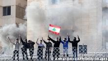 Youths wave a Lebanese flag and gesture from atop a bridge with smoke from flaming tires billowing behind, in the area of Jal el-Dib east of the Lebanese capital Beirut on March 8, 2021 during a protest against the deteriorating value of the local currency and dire economic and social conditions. (Photo by ANWAR AMRO / AFP) (Photo by ANWAR AMRO/AFP via Getty Images)