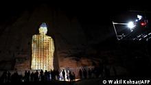 People watch a three-dimensional projection of the 56 metres-high Salsal Buddha at the site where the Buddhas of Bamiyan statues stood before being destroyed by the Taliban in March 2001, in Bamiyan province on March 9, 2021. (Photo by WAKIL KOHSAR / AFP)