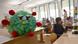 Boneco representando vírus em classe escolar com alunos ao fundo Boneco representando vírus em classe escolar com alunos ao fundo