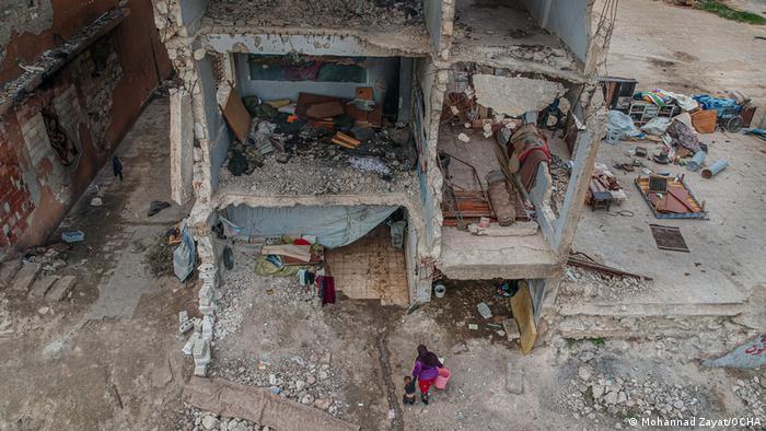 Биниш, април 2020: този кадър, заснет от фотографа Моханад Заят, показва на преден план жена с малката ѝ дъщеря на фона на руините. Двете са намерили подслон в едно разрушено училище в града - едно много опасно укритие. В намиращия се наблизо тотално препълнен лагер за вътрешни бежанци за тях не е имало място. 