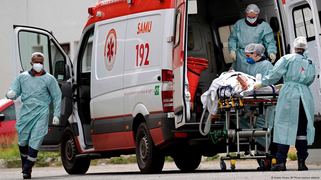 Uma ambulância do Samu com as portas abertas. Do lado de fora, um paciente em cima de uma maca, cercado por profissionais de saúde Uma ambulância do Samu com as portas abertas. Do lado de fora, um paciente em cima de uma maca, cercado por profissionais de saúde