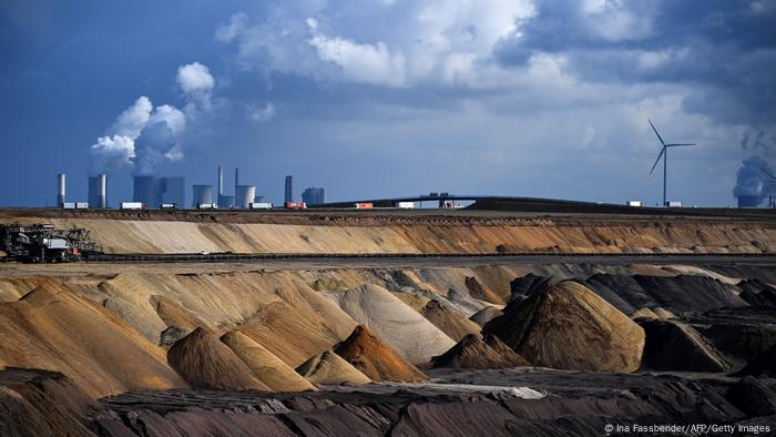 An open-cast mine with chimney stacks puffing smoke in the background