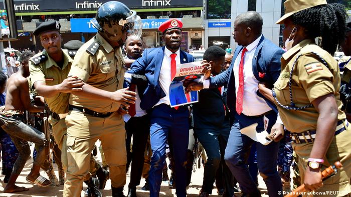 Bobi Wine, a man in a suit and red cap surrounded by police