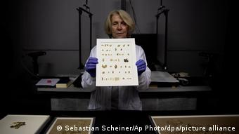 Eine Frau hält einen Rahmen mit kleinen Papyrus-Fragmenten in die Kamera. Sie trägt Plastikhandschuhe und einen Laborkittel