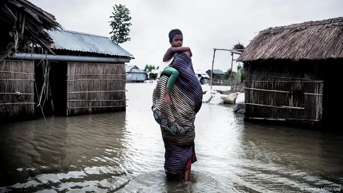 A mother is trying to cross floodwater with her child. 
