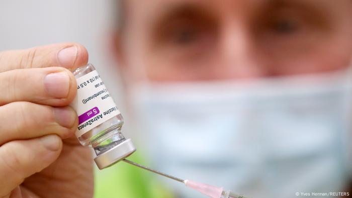 Homem de máscara perfura com seringa um frasco de vacina da AstraZeneca