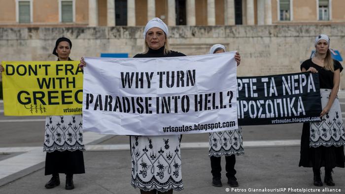 Three women stand in protest holding large signs reading: why turn paradise into hell and don't frack with Greece 