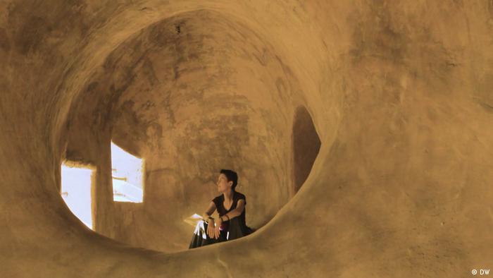 Architect Anna Heringer sitting in a clay buildiing, looking out the window.