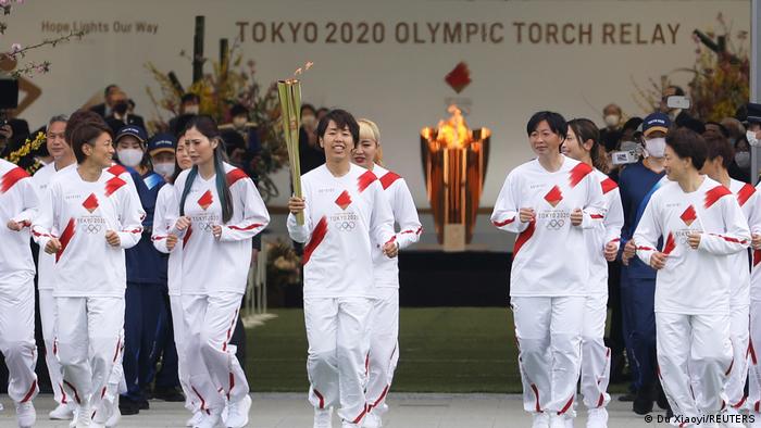 Azusa Iwashimizu (C) and other members of the Japan women's national football team run as torchbearers in the first leg of the torch relay. They are all dressed in white tracksuits