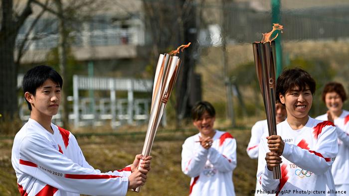 Japanese torchbearer Azusa Iwashimizu, right, passes the flame to high school student Asato Owada, left, at a torch kiss point
