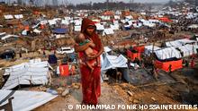 A Rohingya refugee woman carries her child as she looks on in a refugee camp after a massive fire broke out two days ago in Cox's Bazar, Bangladesh, March 24, 2021. REUTERS/Mohammad Ponir Hossain