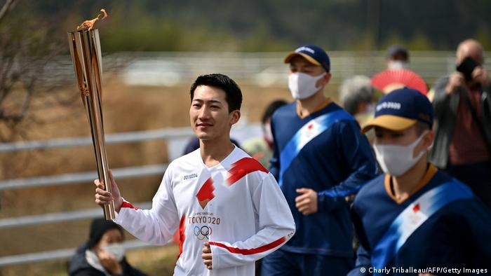 Ryo Matsumoto (G), étudiant à l'Université des sciences du sport de Nippon, porte la flamme dans la ville de Fukushima.