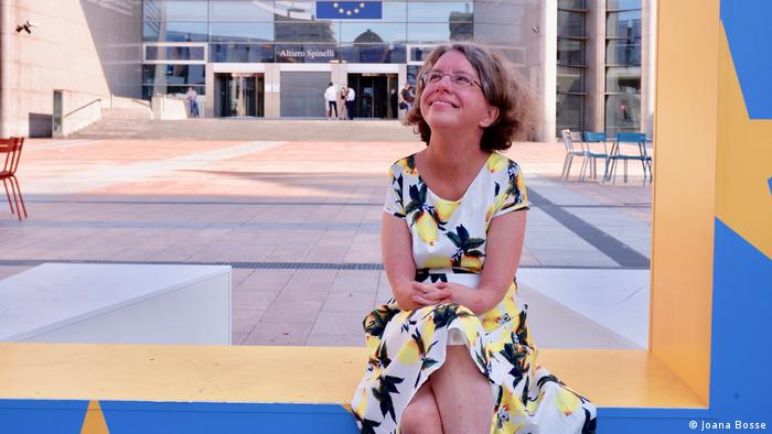 Katrin Langensiepen sitzt auf einer Bank, im Hintergrund eine Fahne der Europäischen Union.