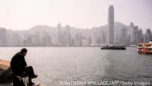 A man sits on a bollard in the Kowloon side of Victoria Harbour, with a view of the Hong Kong Island skyline in the background on January 27, 2021. (Photo by Anthony WALLACE / AFP) (Photo by ANTHONY WALLACE/AFP via Getty Images)